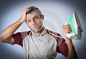 Young crazy desperate and frustrated man doing housework holding iron