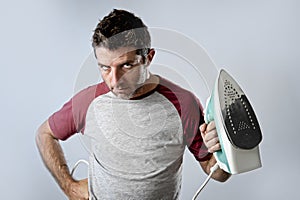 Young crazy desperate and frustrated man doing housework holding iron