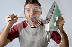 Young crazy desperate and frustrated man doing housework holding iron