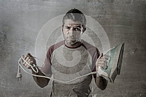 Young crazy desperate and frustrated man doing housework holding iron and cable stressed