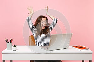 Young crazy joyful woman spreading hands finish working and complete project with pc laptop while sitting at office