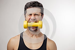 Young crazy sportsman with dumbbell in the mouth