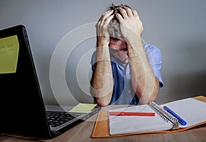 Young crazy stressed and overwhelmed man working messy at office desk desperate with laptop computer covering face with hands frus