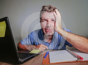 Young crazy stressed and overwhelmed man working messy at office desk desperate with laptop computer crying frustrated and depres