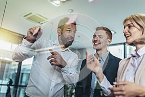 Creative businessman standing with his colleagues writing new ideas on sticky notes over glass wall