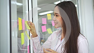 Young Creative businesswoman holding a marker and writing plan and share idea on glass wall with sticky note, Brainstorming and