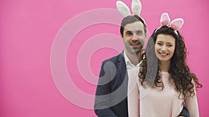 Young creative couple on pink background. With hackneyed ears on the head. During this, two show the gestures of the