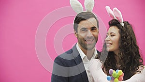 Young creative couple on pink background. With hackneyed ears on the head. During this, the wife holds decorative