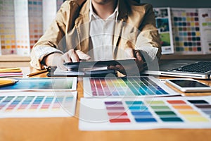 Young creative Graphic designer using graphics tablet to choosing Color swatch samples chart for selection coloring with work too