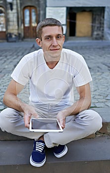 Creative man sitting on sidewalk and using tablet computer