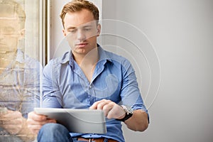 Young creative man sitting at window and using tablet computer