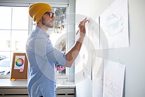 Young creative man writing down ideas on wall full of sticky notes.