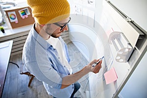 Young creative man writing down ideas on wall full of sticky notes.