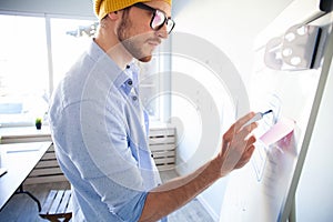 Young creative man writing down ideas on wall full of sticky notes.