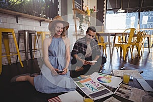 Young creative professionals using technologies while sitting with sheets on floor