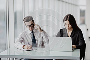 Young creative team brainstorming in the office. Handsome male businessman making call while smiling assistant sitting next to him