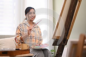 Young creative woman painting picture on canvas with oil paints in her home studio. Leisure activity, creative hobby and