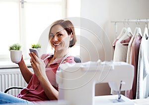 Young creative woman in a studio, using smartphone. A startup of tailoring business.