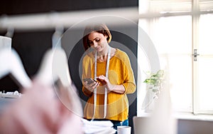 Young creative woman in a studio, using smartphone. A startup of tailoring business.