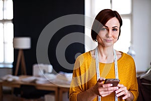 Young creative woman in a studio, using smartphone. A startup of tailoring business.