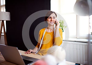 Young creative woman in a studio, using smartphone. A startup of tailoring business.