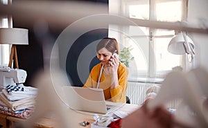 Young creative woman in a studio, using smartphone. A startup of tailoring business.