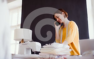 Young creative woman in a studio, using smartphone. A startup of tailoring business.