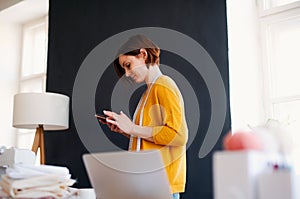 Young creative woman in a studio, using smartphone. A startup of tailoring business.