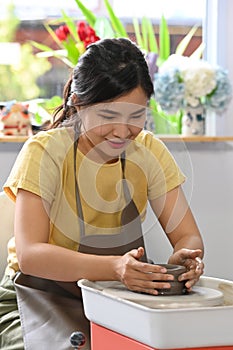 Young creative woman working with clay, creating handicrafter ceramic on the pottery wheel in art workshop. Pottery photo