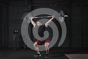 Young crossfit athlete lifting barbell overhead at gym. Man practicing functional training powerlifting workout exercises