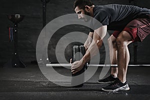 Young crossfit athlete preparing barbell lifting weight at the gym. Magnesia protection dust cloud. Handsome man doing functio