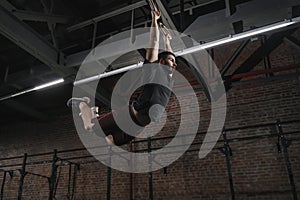 Young crossfit athlete swinging on gymnastic rings doing pull-ups at gym. Workout exercises