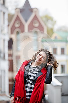 Young curled girl weared in black leather jacket and red scarf on background of old City