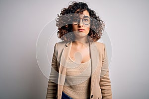 Young curly arab business woman wearing elegant jacket and glasses over white background with serious expression on face