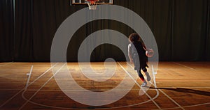 Young curly basketball player plays parquet throws the ball into the basket night darkness training training dribbling