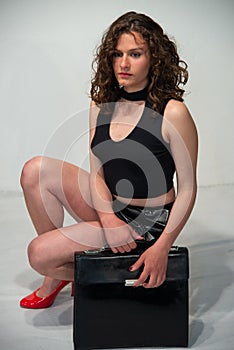 Young curly brunette woman ready to go to the office with her black bag.