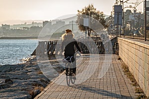 Young curly girl in a yellow hat rides a bicycle at sunset on the promenade road of Maresme, Catalonia, Spain photo