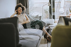 Young curly hair african woman relaxing at home and using mobile phone