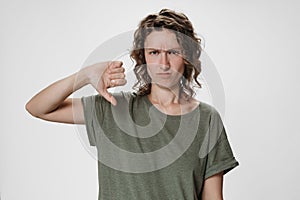 Young curly hair woman frowns face, has displeased gives thumb down gesture