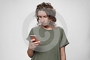 Young curly hair woman holding smartphone looks with great interest at screen