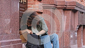 Young curly-haired African American girl sitting on steps outdoors nervously looking in her bag for keys, wallet or