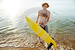 Young curly man with surf board standing in the ocean