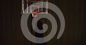 Young curly professional basketball player playing parquet throws the ball into the basket night darkness training