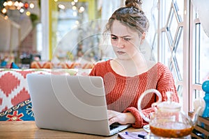 Young curly redhead girl with freckles on the skin with a serious puzzled expression looking at a laptop