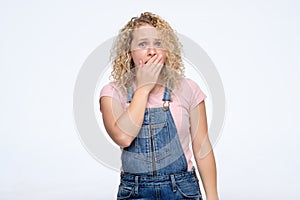 Young curly woman covering her mouth in surprise.
