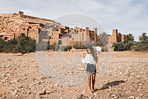 Young curly woman walking on background of Ait-Ben-Haddou. Travel in Morocco