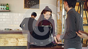 Young customers are ordering takeout coffee in coffeehouse and paying with smart phone while female cashier is accepting