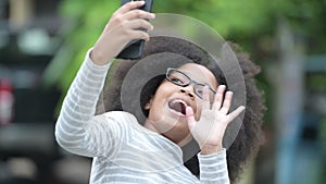 Young cute African girl with Afro hair video calling with phone in the streets outdoors