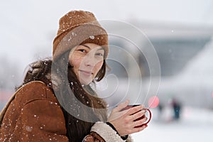 Young cute Asian woman sitting on railway platform with mug of hot tea in snowy winter weather