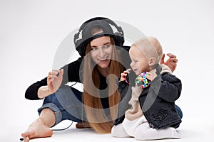 A young cute barefoot mom in a black top, blue jeans and a black baseball cap and her toddler in a black motorcycle